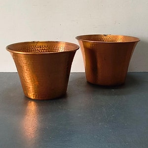 Puede incluir: Dos macetas de cobre martilladas, una más grande que la otra, sobre una superficie gris oscuro.