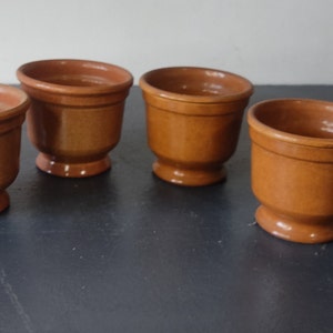 May include: Four small terracotta pots with a brown glaze. The pots have a rounded base and a flared lip.