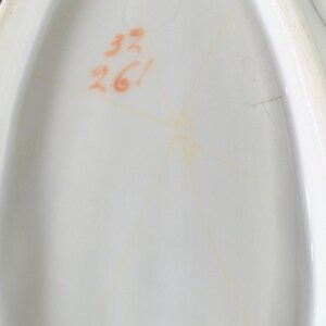 May include: Close-up of a white oval ceramic dish with a handwritten inscription in orange ink that reads "33 26!"