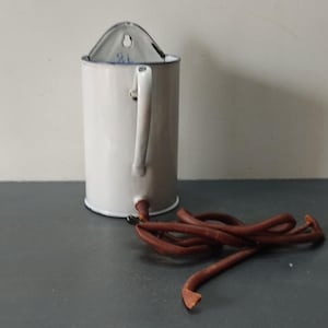 Puede incluir: Jarra de esmalte blanco con asa y tapa. La jarra tiene un agujero en la tapa para colgar. Un cordón de cuero marrón está unido a la parte inferior de la jarra.