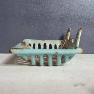 Pu&ograve; includere: Un portasapone vintage in ghisa, di colore azzurro chiaro, con un design traforato decorativo. Il portasapone ha una forma rettangolare ed &egrave; leggermente curvo.