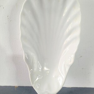 May include: A white ceramic seashell-shaped dish. The dish is smooth and has a glossy finish.