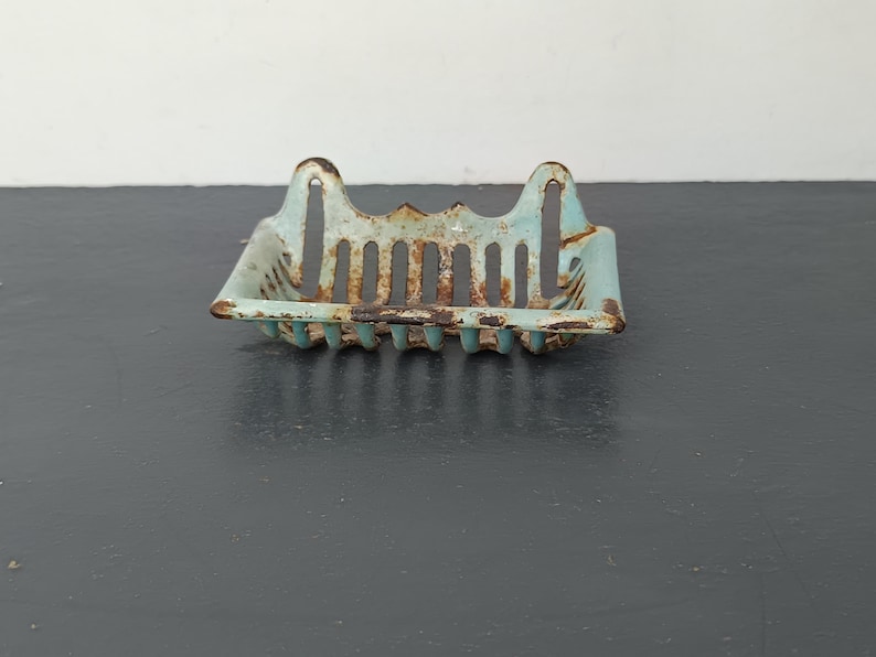 Pu&ograve; includere: Un portasapone vintage in metallo blu chiaro con finitura arrugginita. Il portasapone ha una forma rettangolare con un design traforato decorativo.