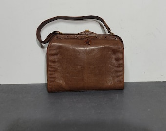 May include: A brown leather handbag with a textured, snakeskin-like pattern. The bag has a top handle and a shoulder strap.