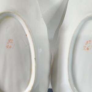 May include: Two white porcelain serving dishes with scalloped edges. The bottom of each dish has an orange stamp that reads "32/261".