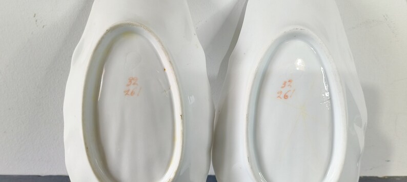 May include: Two white porcelain serving dishes with scalloped edges. The bottom of each dish has an orange stamp that reads "32/261".