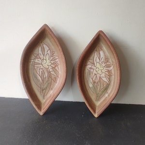 Peut inclure: Deux plats en céramique en forme de feuille avec un glaçage brun et un motif floral blanc.