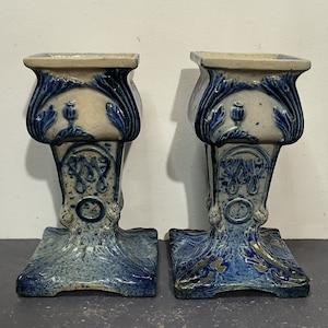 May include: A pair of blue and white ceramic candle holders with intricate floral designs. The holders have a square base and a tall, slender body with a decorative top.