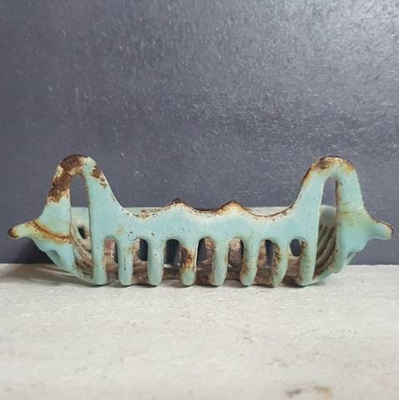 Pu&ograve; includere: Un portasapone vintage in ghisa blu chiaro con un design ondulato decorativo. Il portasapone ha un aspetto rustico e invecchiato con alcune macchie di ruggine.