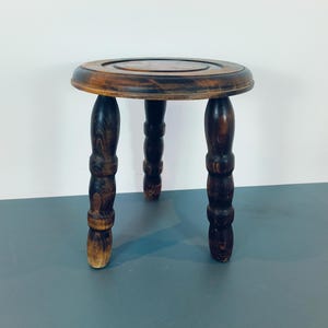 May include: A dark brown wooden stool with a round top and three turned legs.
