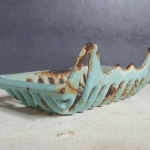 Pu&ograve; includere: Un portasapone vintage in metallo blu chiaro con una finitura arrugginita. Il portasapone ha la forma di una barca con un bordo ondulato e decorativo.