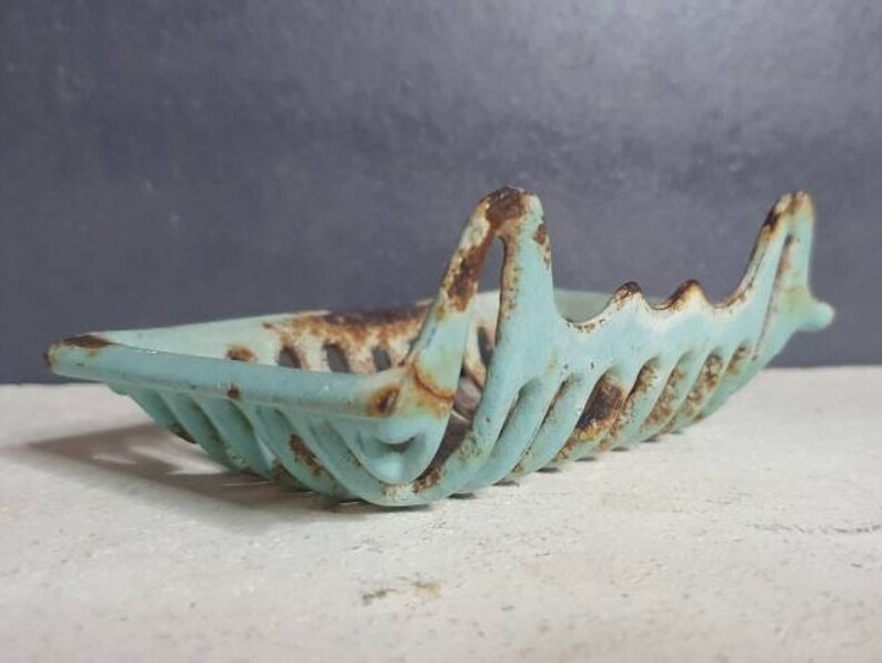 Pu&ograve; includere: Un portasapone vintage in metallo blu chiaro con una finitura arrugginita. Il portasapone ha la forma di una barca con un bordo ondulato e decorativo.