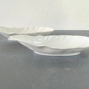 May include: Two white ceramic bowls shaped like seashells. The bowls are smooth and have a glossy finish.