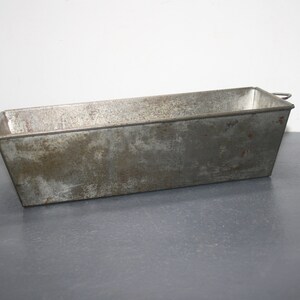 May include: A vintage, rectangular metal loaf pan with a slightly rusted surface. The pan has a handle on one side.
