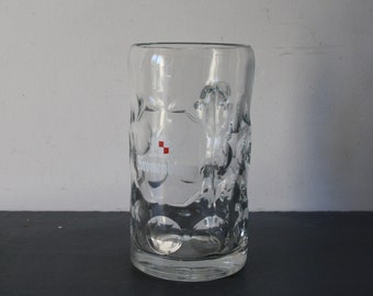 May include: A clear glass beer stein with a textured surface and a white logo that says "Kronenbourg" with a red square in the upper left corner.