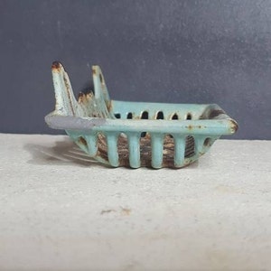 Pu&ograve; includere: Un portasapone vintage in ghisa, di colore azzurro chiaro, con un design traforato decorativo. Il portasapone ha un aspetto leggermente sbiadito e usurato, il che aumenta il suo fascino.