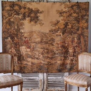 May include: A large tapestry showing a hunting scene with figures on horseback, dogs, and a landscape with trees and mountains. The tapestry is mainly in shades of brown and beige, with a detailed, historical aesthetic.