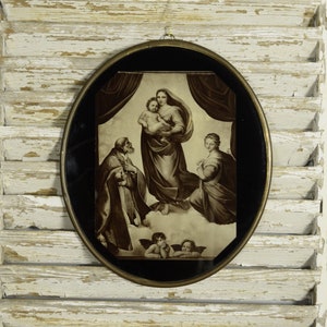 Peut inclure: Une décoration murale ovale présentant une reproduction sépia de la Madone Sixtine. L'image montre un personnage central portant un enfant, entouré de deux personnages agenouillés, avec deux chérubins en bas, le tout dans un cadre en laiton.