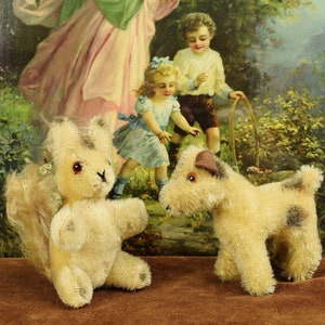 Puede incluir: Dos juguetes de peluche vintage, una ardilla y un terrier, están colocados frente a una impresión vintage de una mujer y dos niños. La ardilla es de color marrón claro con una cola larga y ojos negros. El terrier es de color marrón claro con manchas negras y ojos marrones.