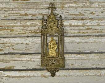 May include: A gold-colored metal religious shrine with a gothic design. The shrine features a relief of the Virgin Mary and child Jesus.