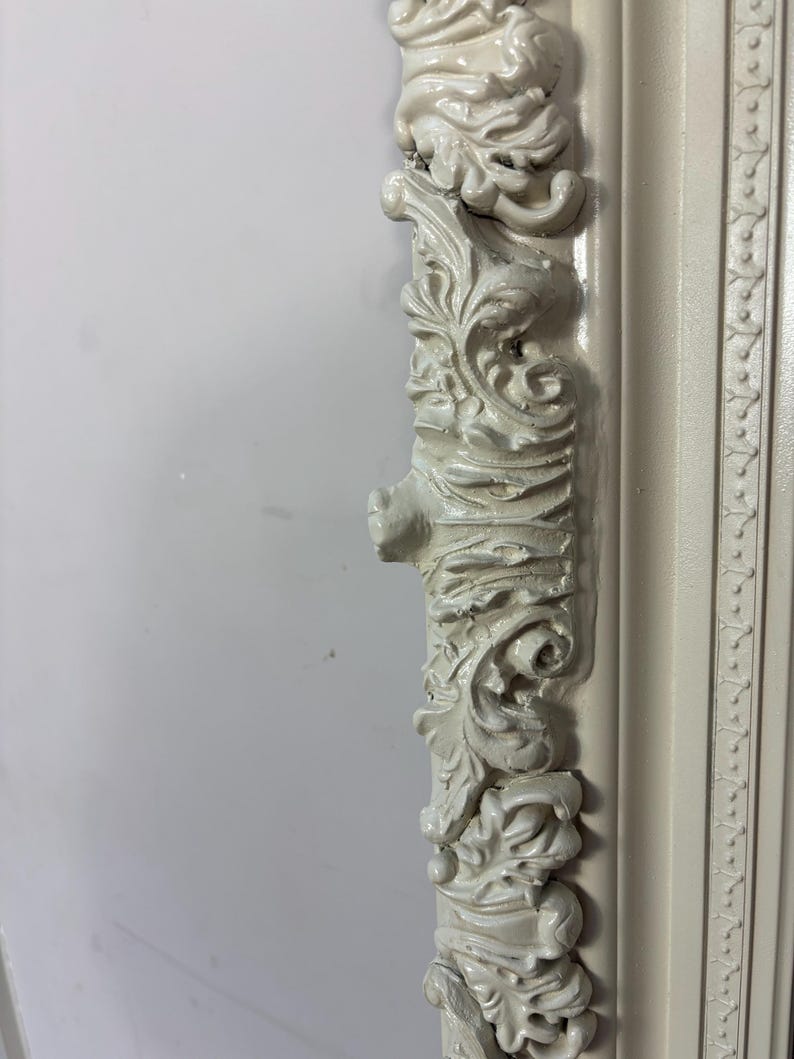 Pu&ograve; includere: Primo piano di una cornice per foto bianca ornata con sculture intricate. La cornice &egrave; in legno e ha una finitura anticata.
