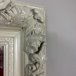Pu&ograve; includere: Una cornice per specchio bianca ornata con intagli intricati e una finitura usurata.