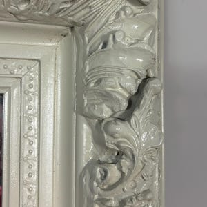Pu&ograve; includere: Una cornice per specchio bianca ornata con intagli intricati e un bordo perlato. La cornice &egrave; in legno e ha una finitura anticata.