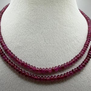 Op de afbeelding: Een dubbele ketting bestaande uit kleine, ronde, dieprode kralen. De kralen zijn dicht op elkaar geregen, waardoor een doorlopend, vloeiend ontwerp ontstaat. De ketting wordt getoond op een witte mannequin.