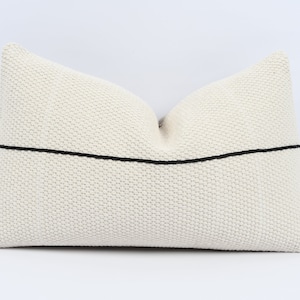 Peut inclure: Un oreiller blanc avec une bande noire au centre. L'oreiller est fait d'un tissu texturé.