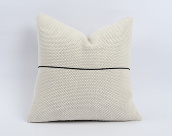 May include: A white knitted cushion with a black stripe across the centre.