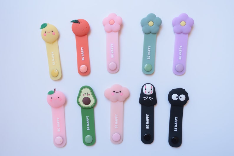 May include: Ten colorful cable organizers with different cartoon characters. Each organizer has the text "BE HAPPY" printed on it.