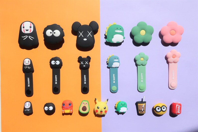May include: Assortment of colorful cartoon character cable organizers.  The characters include No Face, Totoro, Mickey Mouse, a dinosaur, a flower, a Pikachu, an avocado, a frog, a boba tea cup, and a Coca-Cola can.  The organizers are made of silicone and have the words "Be Happy" printed on them.