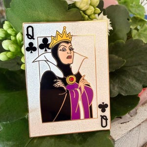 Op de afbeelding: Een rechthoekige pin met de boze koningin uit Sneeuwwitje als de klaveren vrouw speelkaart. De pin heeft een gouden rand en een zilveren glitter achtergrond. De boze koningin is afgebeeld in haar kenmerkende zwarte en paarse kleding, met een gouden kroon.