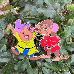 Op de afbeelding: Twee emaillepins met de personages uit de Disney-film De Grote Muizendetective. Basil van Baker Street draagt een rode jas en een bruine hoed. Het andere personage, Dr. Dawson, draagt een gele jas en een paarse hoed.