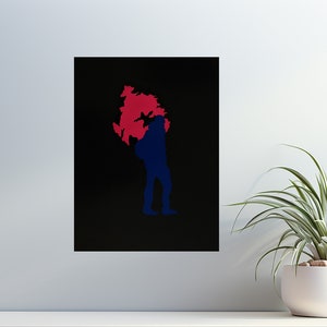 Può includere: Una stampa artistica incorniciata con una silhouette blu di una persona che trasporta una forma rossa e blu su sfondo nero. L'opera d'arte è esposta su una superficie bianca con una pianta in vaso in primo piano.