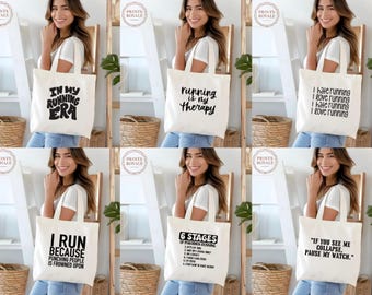 Puede incluir: Una colección de bolsas de lona blancas con varios diseños de texto en negro. Los diseños incluyen frases como "In My Running Era", "Running is My Therapy" y citas de running humorísticas. Las bolsas son sostenidas por una persona.