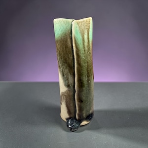 Puede incluir: Un jarrón de cerámica hecho a mano con un diseño abstracto único. El jarrón presenta una forma vertical dividida con una mezcla de colores, incluyendo verde, marrón y crema. La base tiene un acento oscuro y moteado. El jarrón mide aproximadamente 20 cm de alto.