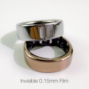 Op de afbeelding: Twee slimme ringen, één zilverkleurig en één bronskleurig, op elkaar gestapeld. De zilverkleurige ring ligt bovenop, de bronzen ring eronder. De tekst "Invisible 0.15mm Film" staat onderaan. De film is 0,15 mm dik.