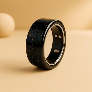 Peut inclure: Une bague intelligente noire avec un motif étoilé sur le dessus. Elle possède un anneau intérieur argenté et deux petits capteurs circulaires. Un accessoire technologique portable.