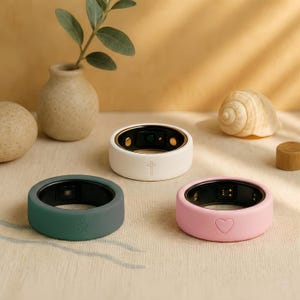 May include: Three smart rings in white, teal, and pink. The white ring has a gold rim and a cross symbol. The teal ring has a sun symbol, and the pink ring has a heart symbol. All rings have a black interior.