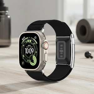 May include: A silver smartwatch with a black strap, showing the time as 10:09. The watch face displays data, including 46% battery. The strap has a magnetic clasp. The watch is on a wooden surface.