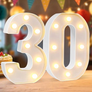 May include: Two white marquee-style number lights forming the number 30. Each digit features a smooth white frame and is illuminated by several warm white LED bulbs arranged along the front face of the numbers, creating a bright glow.