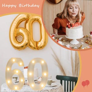 May include: A birthday celebration featuring a woman blowing out candles on a cake. Gold foil balloons in the shape of the number 60 are displayed. A lighted number 60 is on a table, with "Happy Birthday" written at the top.