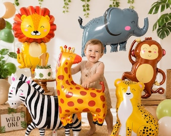 May include: A collection of animal-shaped foil balloons including a lion, elephant, monkey, giraffe, zebra, and cheetah. The balloons feature cartoon-style faces and vibrant colors. A small cake with a number one topper sits on a wooden stand.