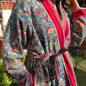 May include: A teal blue and red floral print robe with a long sleeve and a tie belt. The robe has a red trim and white piping.