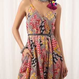 Może przedstawiać: Sukienka bez rękawów w czerwono-żółto-czarne wzory z czarnym paskiem. Sukienka ma dekolt w kształcie litery V i rozkloszowaną spódnicę.