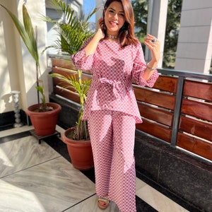 May include: A pink and white patterned pantsuit with a tie waist. The pantsuit is made of a lightweight fabric and has a relaxed fit.