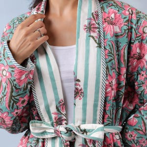 May include: A floral print robe in shades of teal and pink, featuring a striped collar and tie. The robe's design includes large pink flowers and green leaves on a teal background. The collar and tie have white and teal stripes.