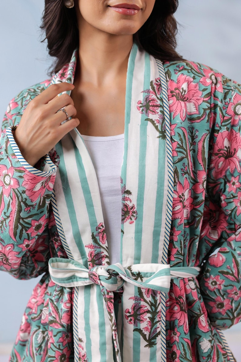 May include: A floral print robe in shades of teal and pink, featuring a striped collar and tie. The robe's design includes large pink flowers and green leaves on a teal background. The collar and tie have white and teal stripes.