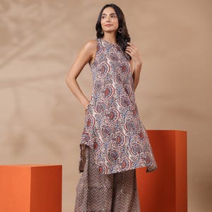 May include: A sleeveless tunic and wide-leg pants set. The tunic features a cream-colored base with a paisley pattern in red and blue. The pants have a complementary brown and cream pattern. The model is wearing brown sandals.